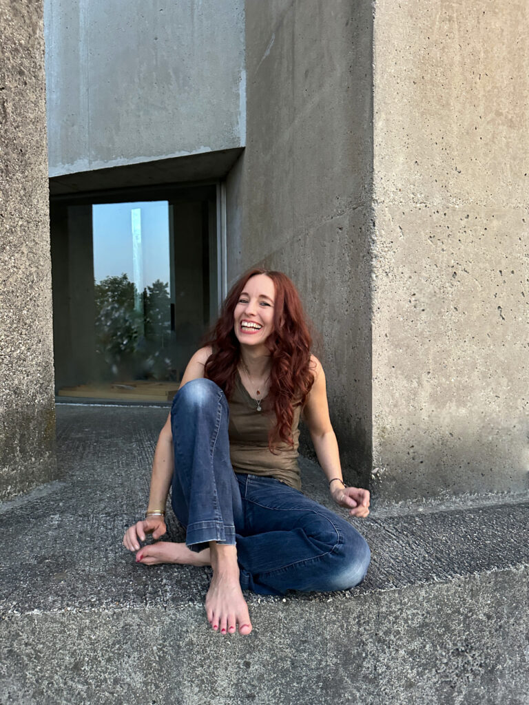 Iris Feige Psychologische Beraterin und Humanenergetikerin sitzt lachend auf einem modernen Gebäude